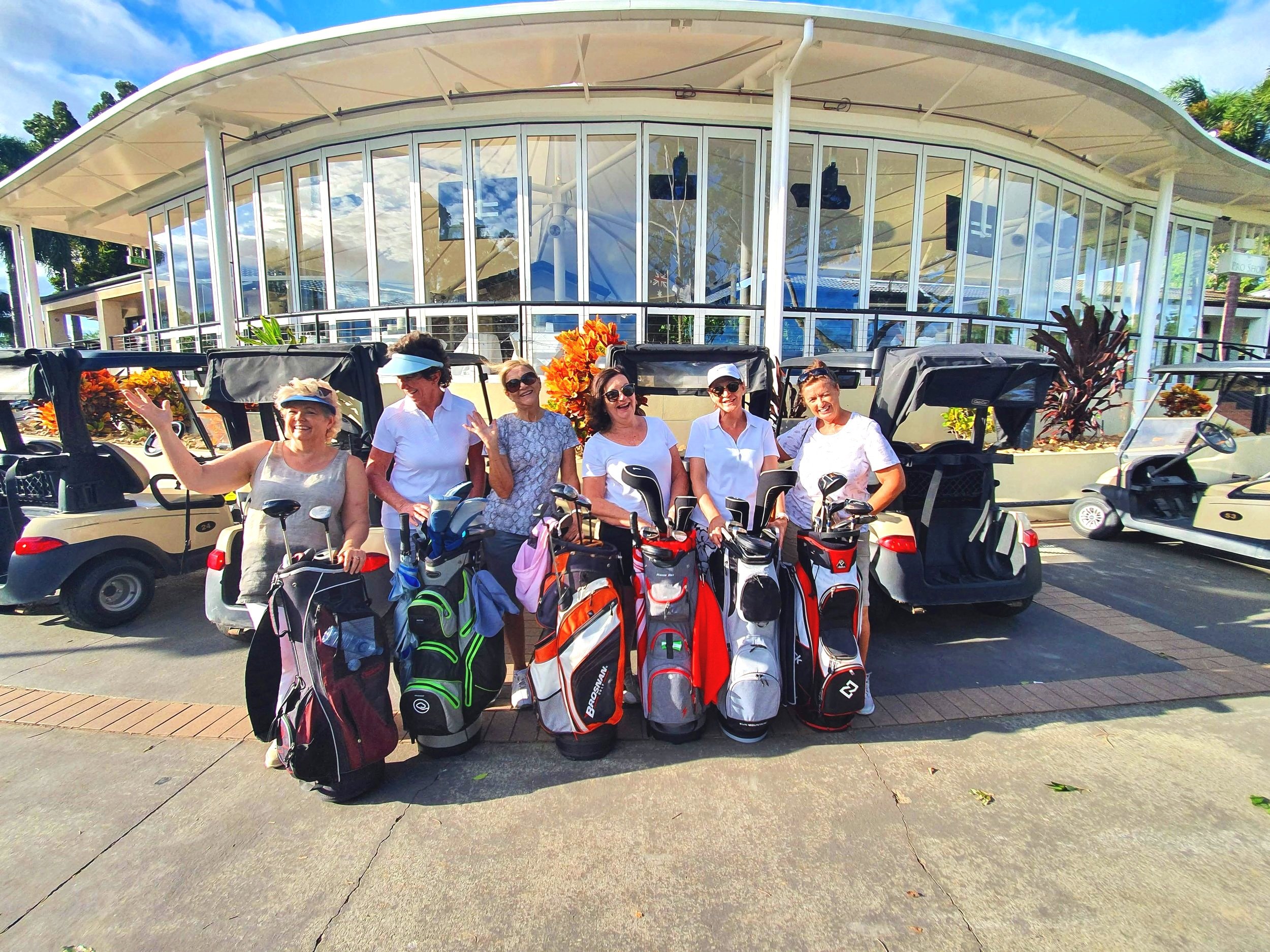 Group of women with golf bags in front of a modern building and golf carts. GOLF COACHING, PAUL WILLIAMSON GOLF