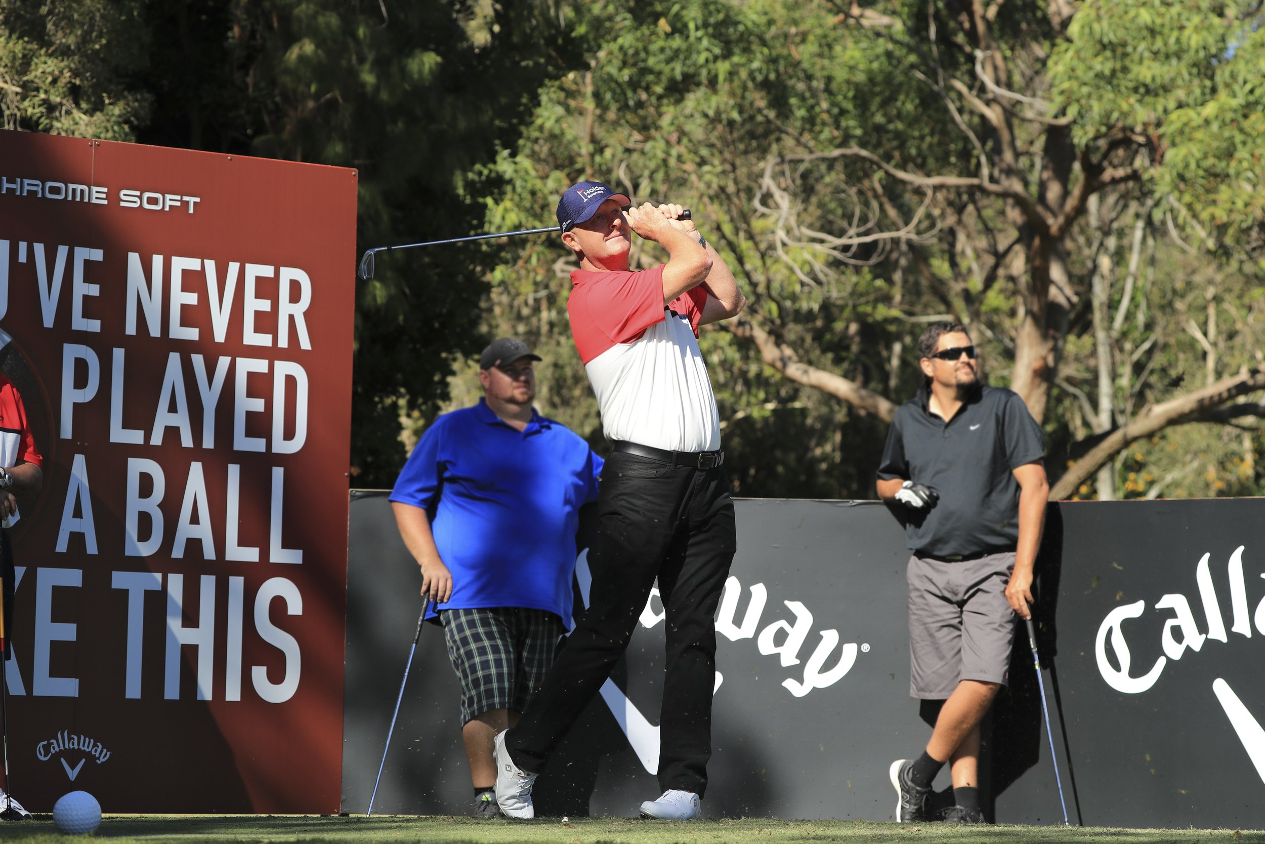 Golfer taking a swing at a golf course with spectators nearby, in front of a Callaway advertisement.