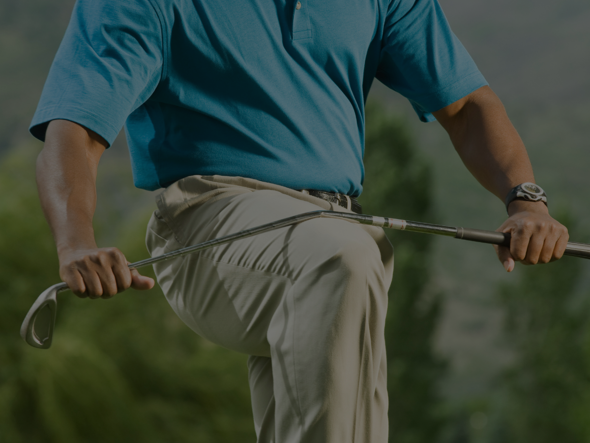 Golfer in blue shirt and beige pants holding golf club, knee raised.