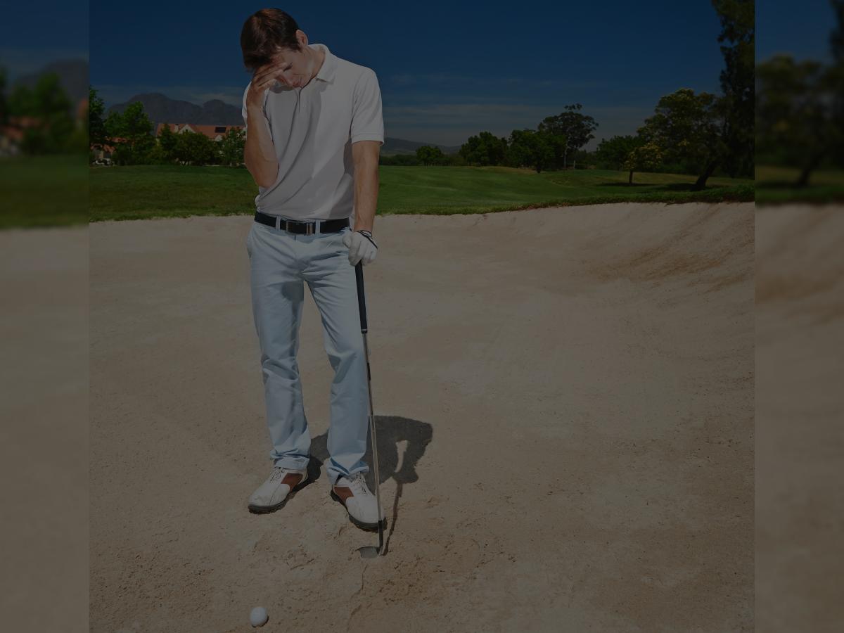 Golfer looking frustrated in sand trap with golf club and ball